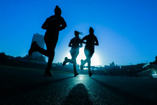 Runners silhouetted against the morning sun on a paved road